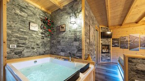 A stone-walled bathroom with a large bathtub, wooden beams, and a stone fireplace. - B_AL RANCH Wellness Cortina, Lake Cadore, Dolomites (Pozzale)