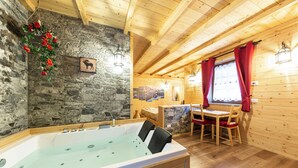 A wooden cabin interior with a stone wall, a wooden dining table, and a hot tub. - B_AL RANCH Wellness Cortina, Lake Cadore, Dolomites (Pozzale)