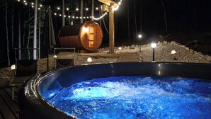 A hot tub surrounded by a deck, with a wooden barrel and string lights in the background. - B_AL RANCH Wellness Cortina, Lake Cadore, Dolomites (Pozzale)