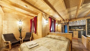 A wooden cabin with a bed, two chairs, a small table, a vase with flowers, and a kitchen area. - B_AL RANCH Wellness Cortina, Lake Cadore, Dolomites (Pozzale)