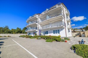 Un immeuble à plusieurs étages doté de balcons, d’un espace de stationnement et surplombant un ciel d’un bleu limpide.