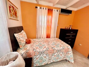 A bedroom with a patterned bedspread, a headboard, a dresser, and a wall-mounted air conditioner. - Luxury Home Hughenden Kingston (Kingston)