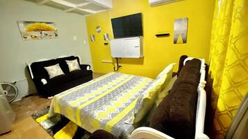 A room with a bed, a black sofa, a small table, and a wall-mounted TV.