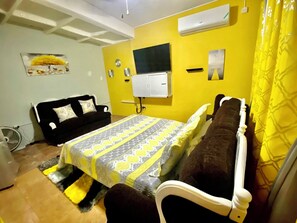 A room with a bed, a black sofa, a small table, and a wall-mounted TV. - Luxury Home Hughenden Kingston (Kingston)