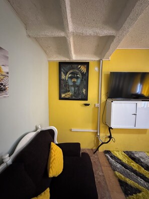 A room with a yellow wall, a black and white sofa with a yellow pillow, a TV on a white cabinet, and a framed artwork above the sofa. - Luxury Home Hughenden Kingston (Kingston)
