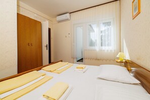 Ein Hotelzimmer mit einem Bett, einer Nachttischlampe, einem Fenster mit Vorhängen und einer Klimaanlage.