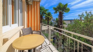 A balcony with a table and chair, a striped curtain, and a view of palm trees and buildings. - Dog-friendly apartment just 260 metres from the beach with sea views, barbecue (Dramalj)