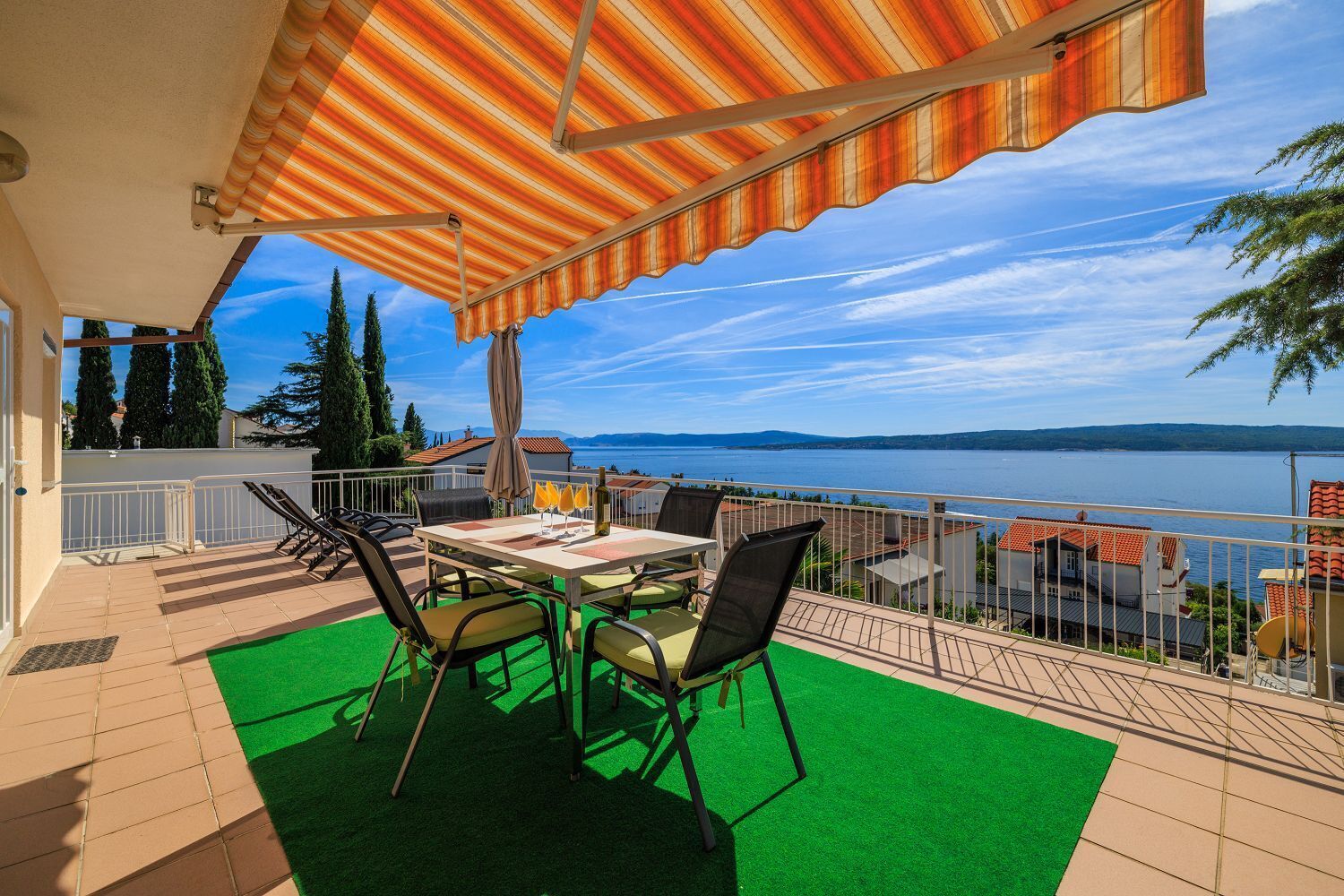 A terrace with a table and chairs, a view of the sea, and a green artificial turf area.