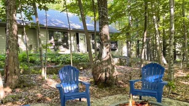 Ein Garten mit zwei blauen Adirondack-Stühlen, einer Feuerstelle und einem Haus im Hintergrund.