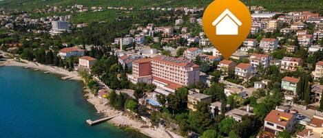 An aerial view of a coastal town with a prominent hotel featuring multiple floors and a red roof, surrounded by residential buildings and a coastline.