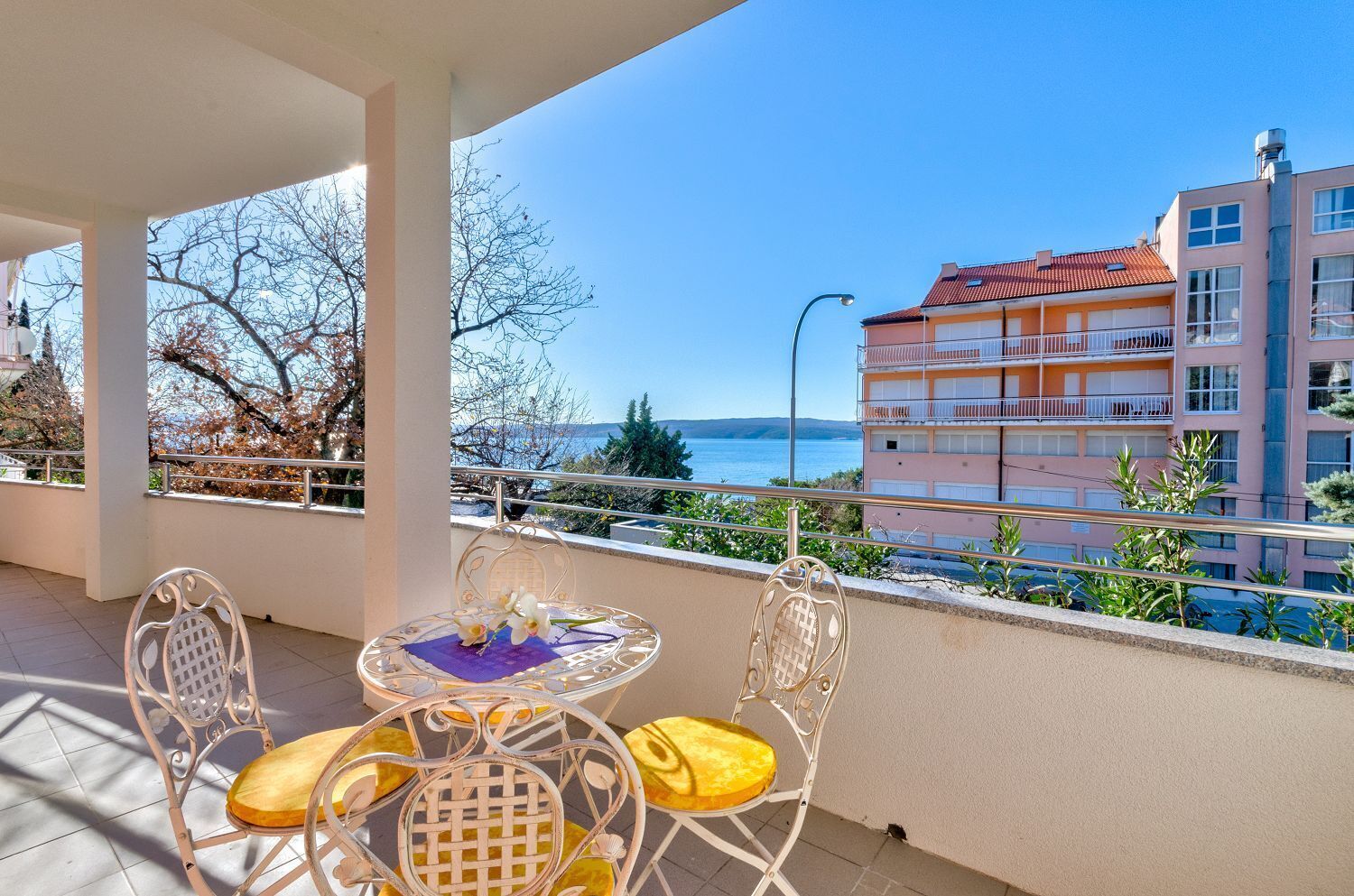A balcony with a table and chairs, overlooking a body of water and a building with balconies.