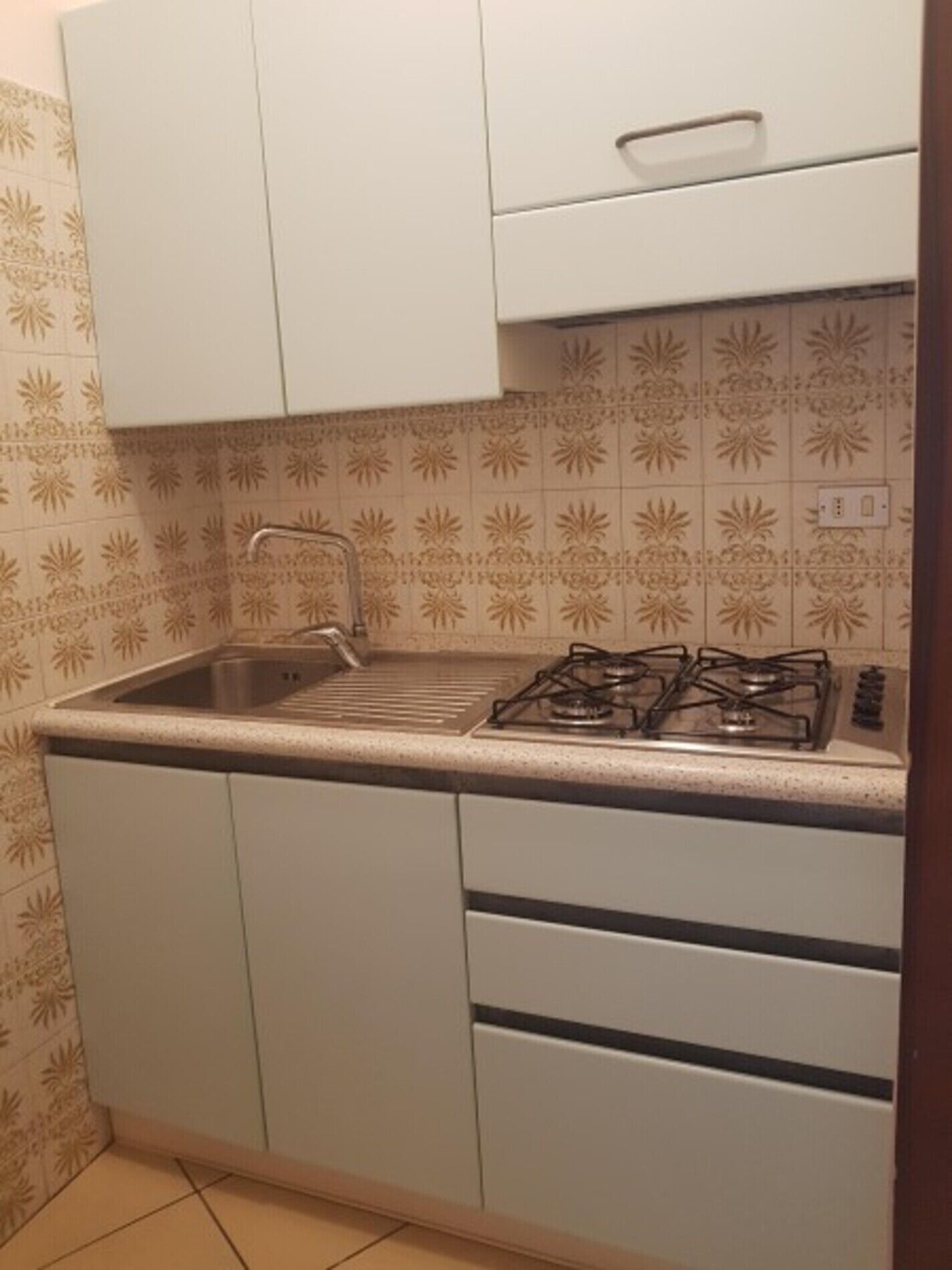 Une cuisine de taille réduite, équipée d’une cuisinière à gaz, d’un évier et de meubles blancs.
