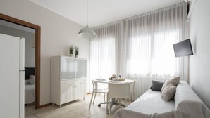 A modern, well-lit room with a bed, a dining table, and a TV mounted on the wall. - Studio Apartment With Pool in Jesolo (Jesolo)