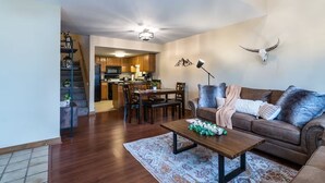 A spacious living room with a brown leather sofa, a coffee table, and a patterned rug. A dining area with wooden chairs and a table is visible in the background. - Rustic In-Town Retreat | Pool | Hot Tub (Durango)