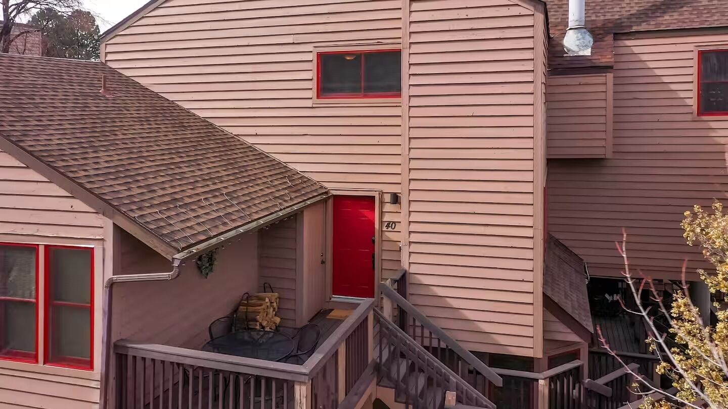 A two-story house with a red door, a small porch with a table and chairs, and a visible number '40' on the side.