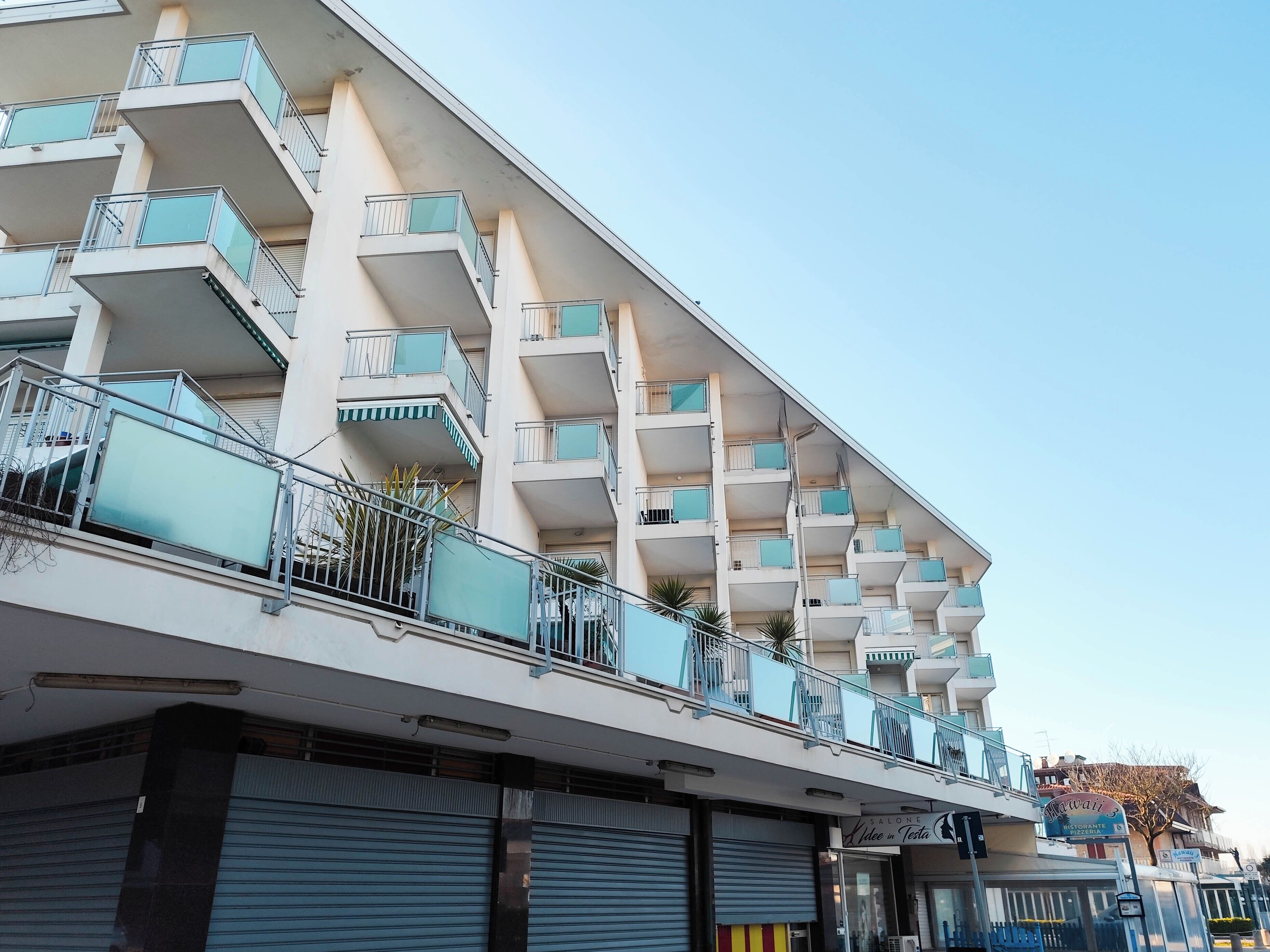 Un immeuble à plusieurs étages, doté de balcons, d’une enseigne de restaurant et de volets fermés au rez-de-chaussée.