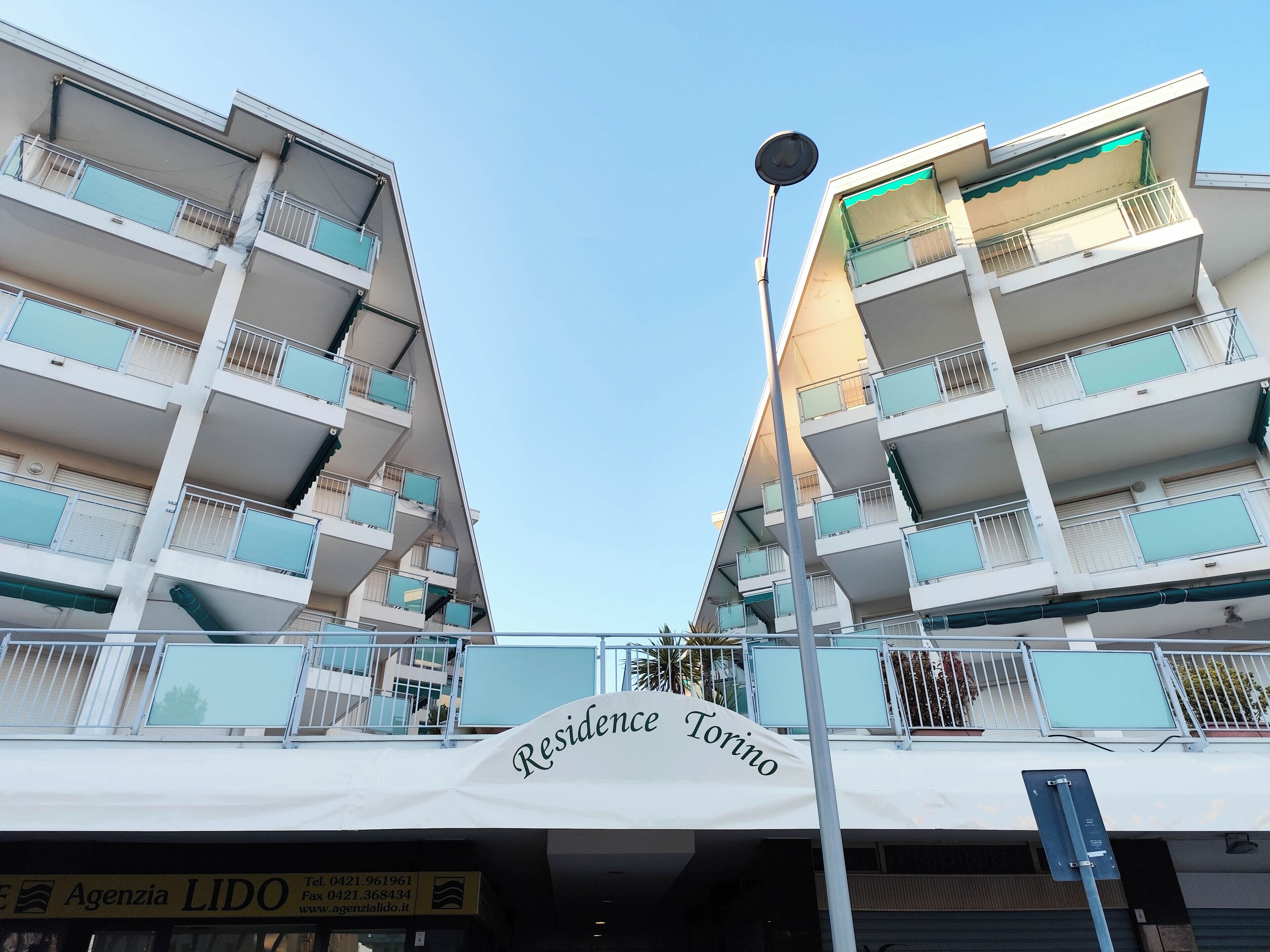 A multi-story residential building with balconies, a sign reading "Residence Torino," and a street lamp.