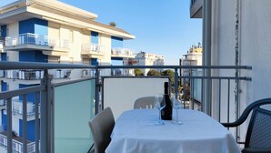 A balcony with a table set for two, a bottle of wine, and two glasses. The balcony overlooks a row of buildings with balconies. - Cozy Flat With Pool Near the Beach (Jesolo)