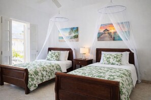 A room with two wooden beds, each with a canopy and floral bedding. There is a nightstand with a lamp between the beds, and a painting of a sunset on the wall. - Mullins Beach Villa - Luxury with Private Spa Pool (Battaleys Mews)
