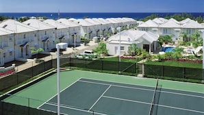 Une rangée de bâtiments blancs, avec un court de tennis au premier plan.