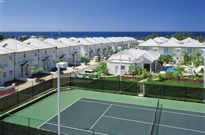 A row of white buildings with a tennis court in the foreground. - Mullins Beach Villa - Luxury with Private Spa Pool (Battaleys Mews)