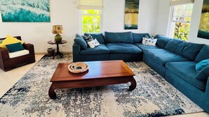Un salon avec un canapé d’angle bleu foncé, une table basse en bois, un tapis à motifs et un tableau accroché au mur.