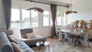Una sala moderna con un sofá gris, una mesa de comedor con sillas y un ventanal con cortinas.