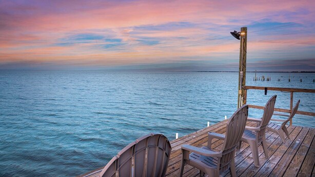 Une terrasse en bois avec des chaises, donnant sur une mer calme au coucher du soleil.