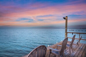A wooden deck with chairs overlooking a calm sea at sunset. - Copano Bay Waterfront | Private Fishing Pier & Kayaks (Rockport)