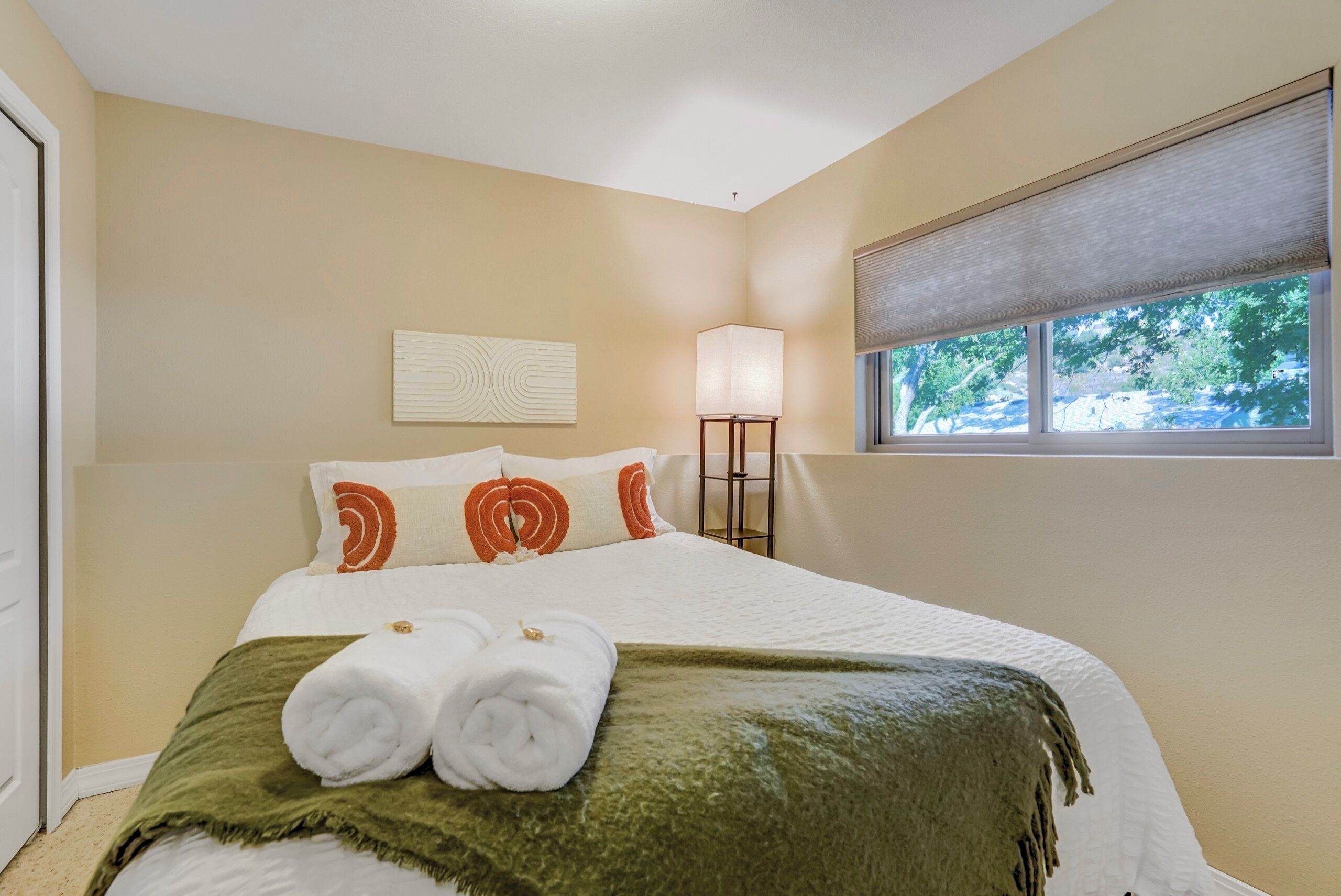 A hotel room with a bed, a window with a view, a bedside lamp, and a wall decoration.