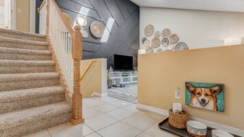 Un escalier avec une rampe en bois menant à un palier où se trouvent un téléviseur à écran plat, un panier et un tableau représentant un chien.