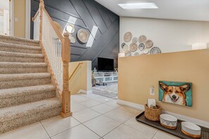 A staircase with a wooden handrail leading to a landing with a flat-screen TV, a basket, and a painting of a dog. - Dogs Off-Leash in the Fenced Yard: 4BR Home, Sleeps 9 (Colorado Springs)