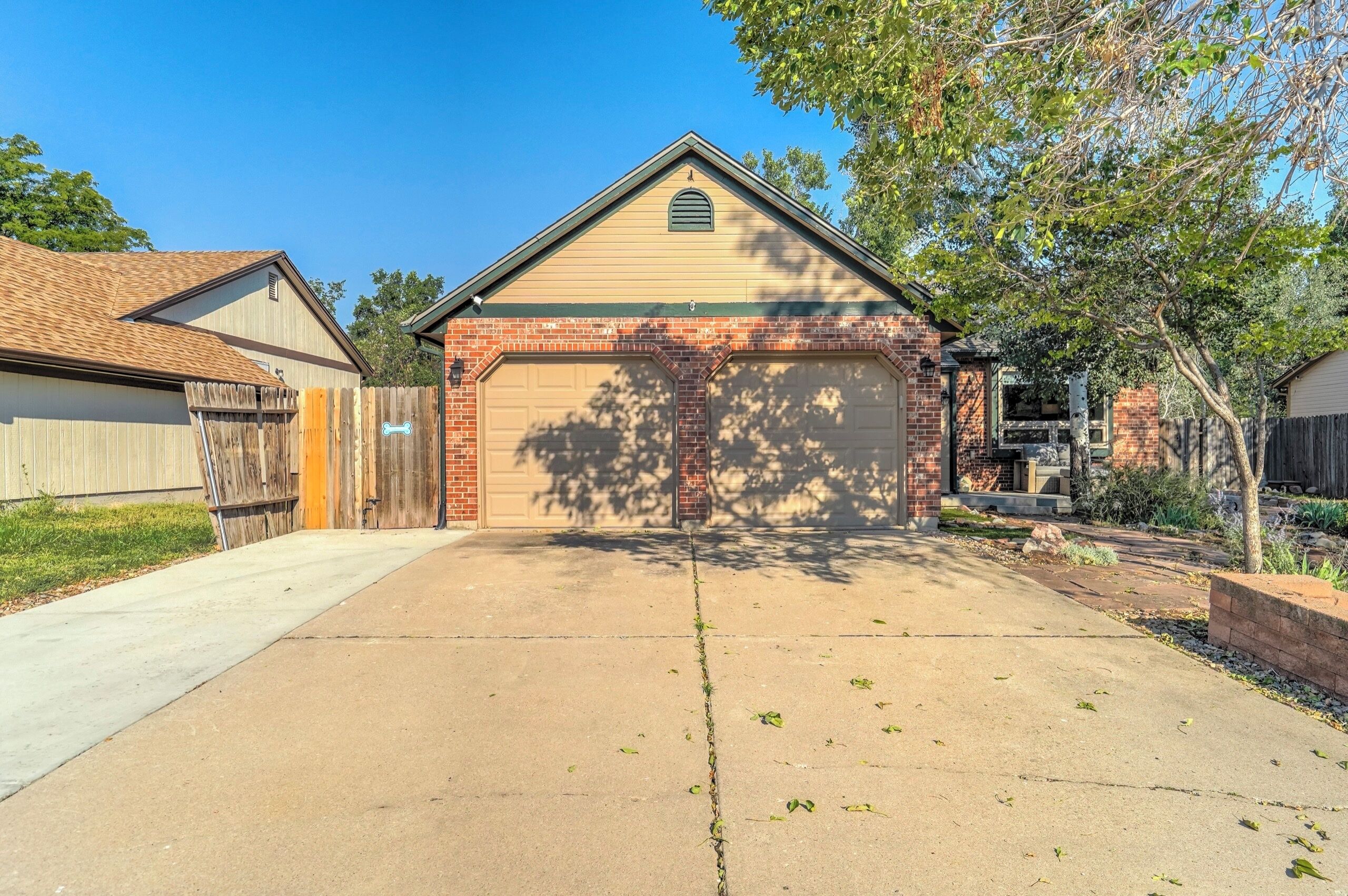 A single-story residential garage with a brick facade, a clear driveway, and a wooden fence on the left.