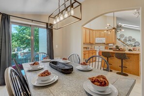 A dining area with a table set for four, a kitchen with wooden cabinets, and a view of the outdoors.