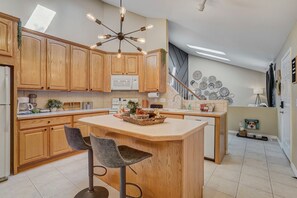 A modern kitchen with wooden cabinets, a central island with bar stools, a built-in microwave, and a unique ceiling light fixture. - Dogs Off-Leash in the Fenced Yard: 4BR Home, Sleeps 9 (Colorado Springs)