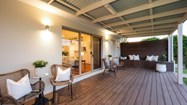 Un patio exterior con mobiliario de mimbre, una zona cubierta y vistas al interior de la casa.