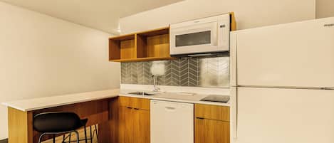 A compact kitchen with a microwave, dishwasher, and a small bar stool.