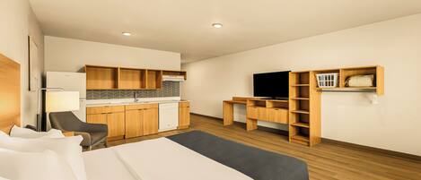 Une chambre d’hôtel équipée d’un lit, d’un bureau, d’une chaise, d’une kitchenette et d’une télévision.