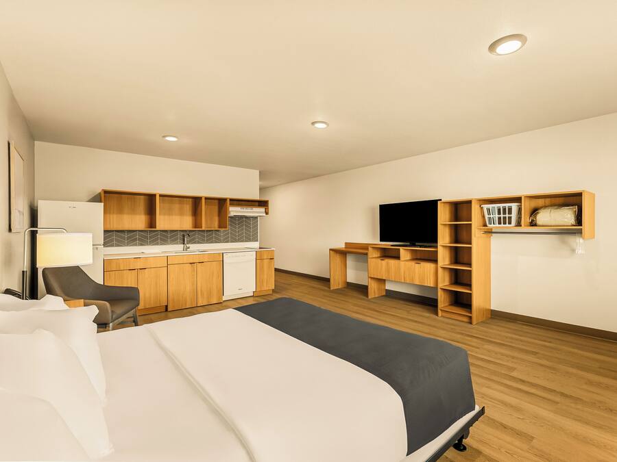 A hotel room with a bed, desk, chair, kitchenette, and TV.