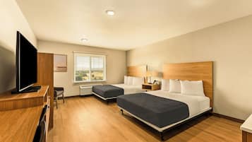 A hotel room with two beds, a desk with a TV, a window with blinds, and a wooden headboard.
