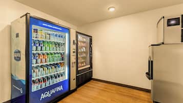 Um quarto com piso de madeira, uma geladeira e duas máquinas de venda automática identificadas como 'AQUAFINA'.