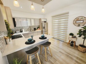 A modern kitchen with a central island, bar stools, a built-in oven, and a refrigerator. - Playa Cañones / Margarita Beach House / Private / Heated Pool (Aguada)