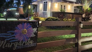 A modern house with a well-lit entrance, surrounded by lush greenery and palm trees. - Playa Cañones / Margarita Beach House / Private / Heated Pool (Aguada)
