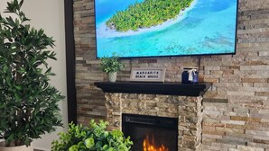 A living room with a stone fireplace, a flat-screen TV, and a sign reading "Margarita Beach House". - Playa Cañones / Margarita Beach House / Private / Heated Pool (Aguada)