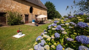 A rustic stone building with a thatched roof, a patio with outdoor furniture, and a garden with hydrangea flowers.