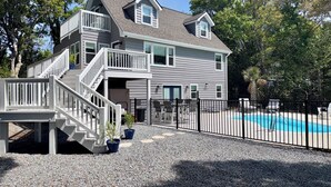 Une maison à deux étages avec une terrasse à l’avant, une piscine et une allée gravillonnée.