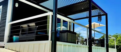 A modern outdoor patio with a covered seating area, a white fence, and a clear blue sky.