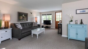 A living room with a grey sofa, a white coffee table, a TV stand, a light blue cabinet, and a painting on the wall. - Rush Pond Retreat at Goose Rocks Beach (Kennebunkport)