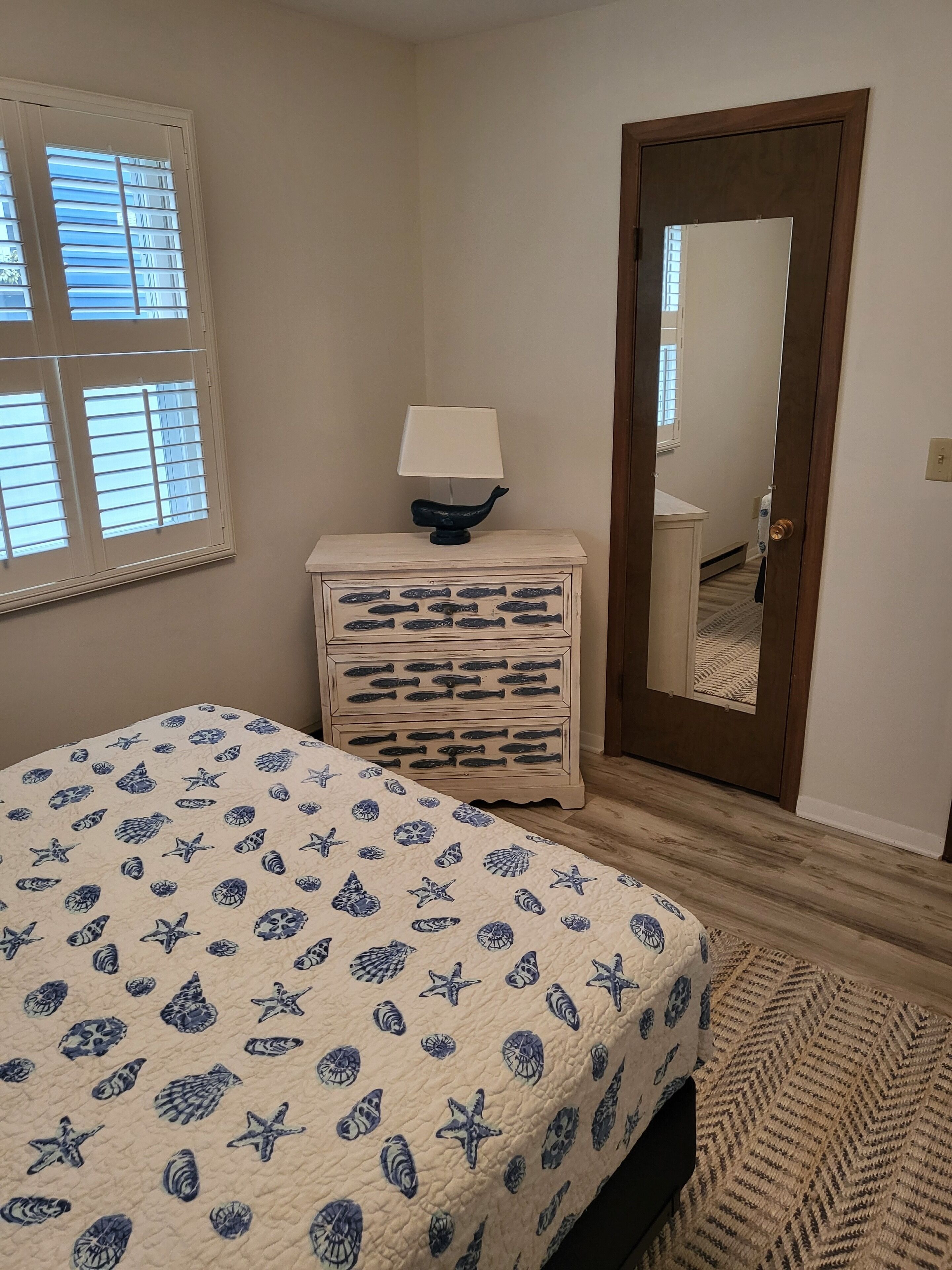 A bedroom with a bed, a nightstand, a lamp, a dresser, and a door.
