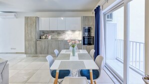 A modern kitchen with a built-in oven and microwave, a dining area with a table and chairs, and a balcony with a view. - Central Msida | Modern, Bright & Comfortable (Msida)